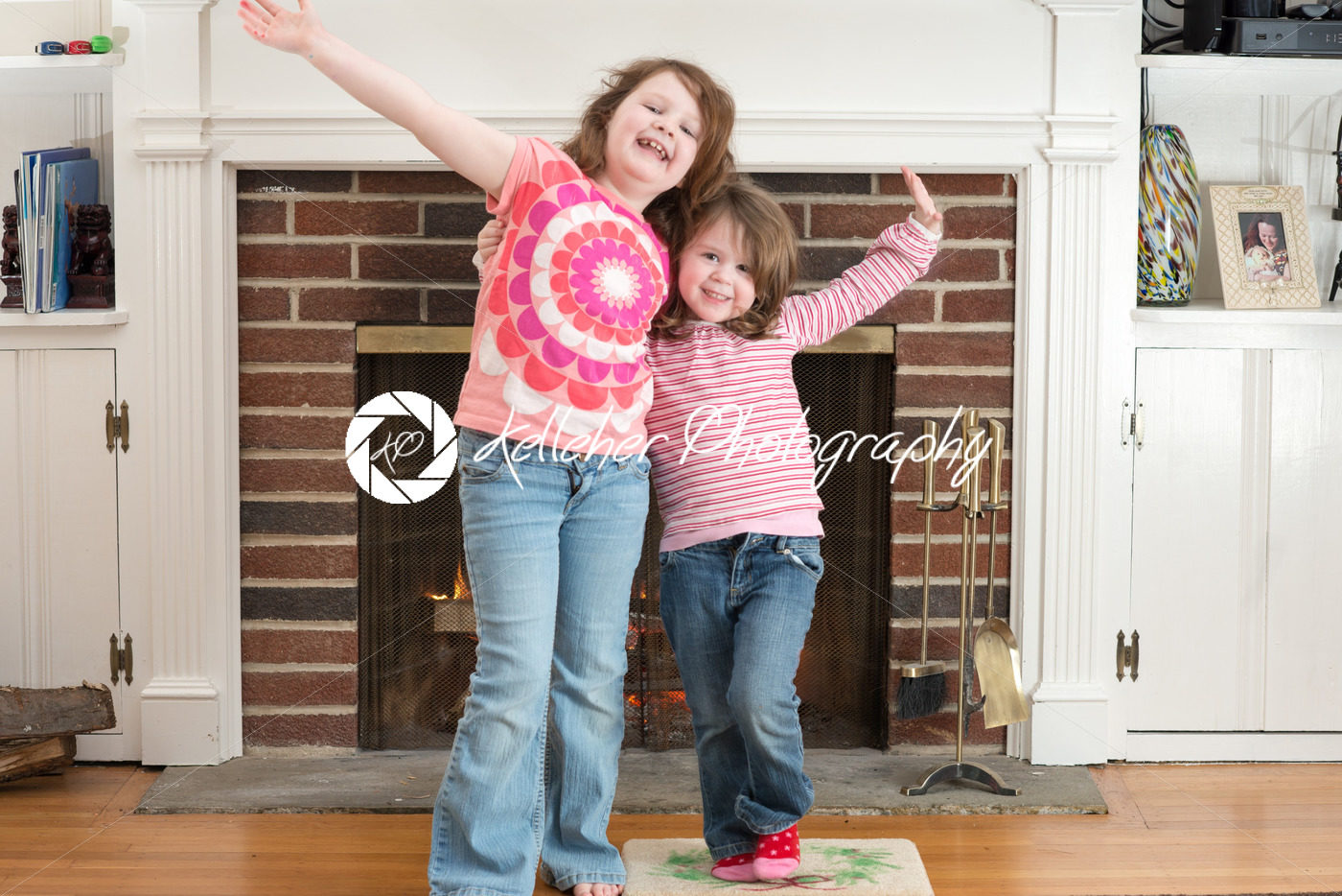 Portrait of a two young smiling sibling girls in front of a fireplace dressed for valentine’s day - Kelleher Photography Store