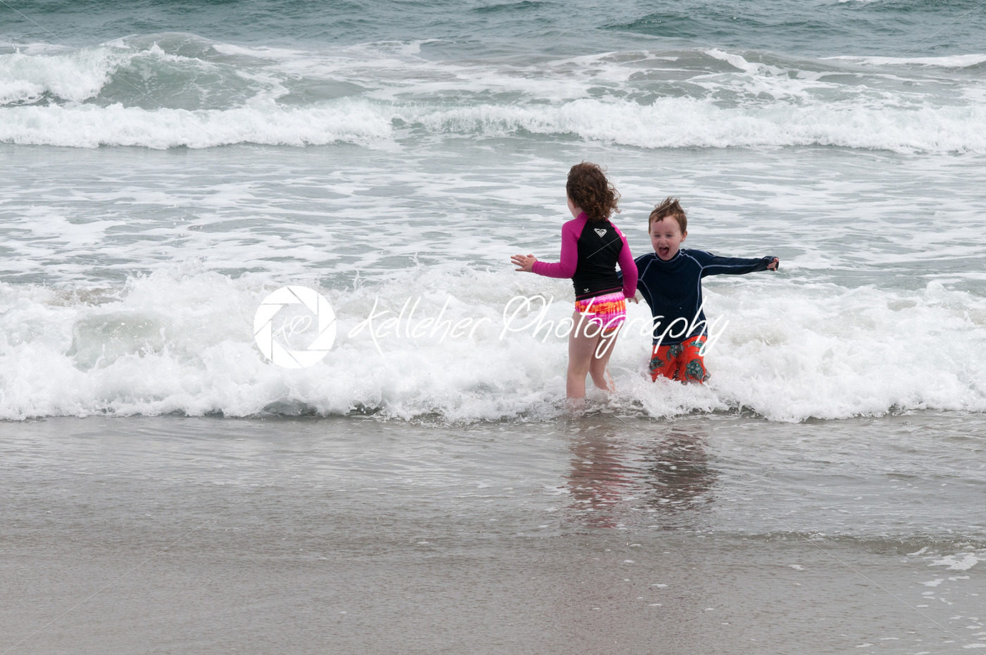 Young cute little boy and girl playing at the seaside running into the surf on a sandy beach in summer sunshine - Kelleher Photography Store