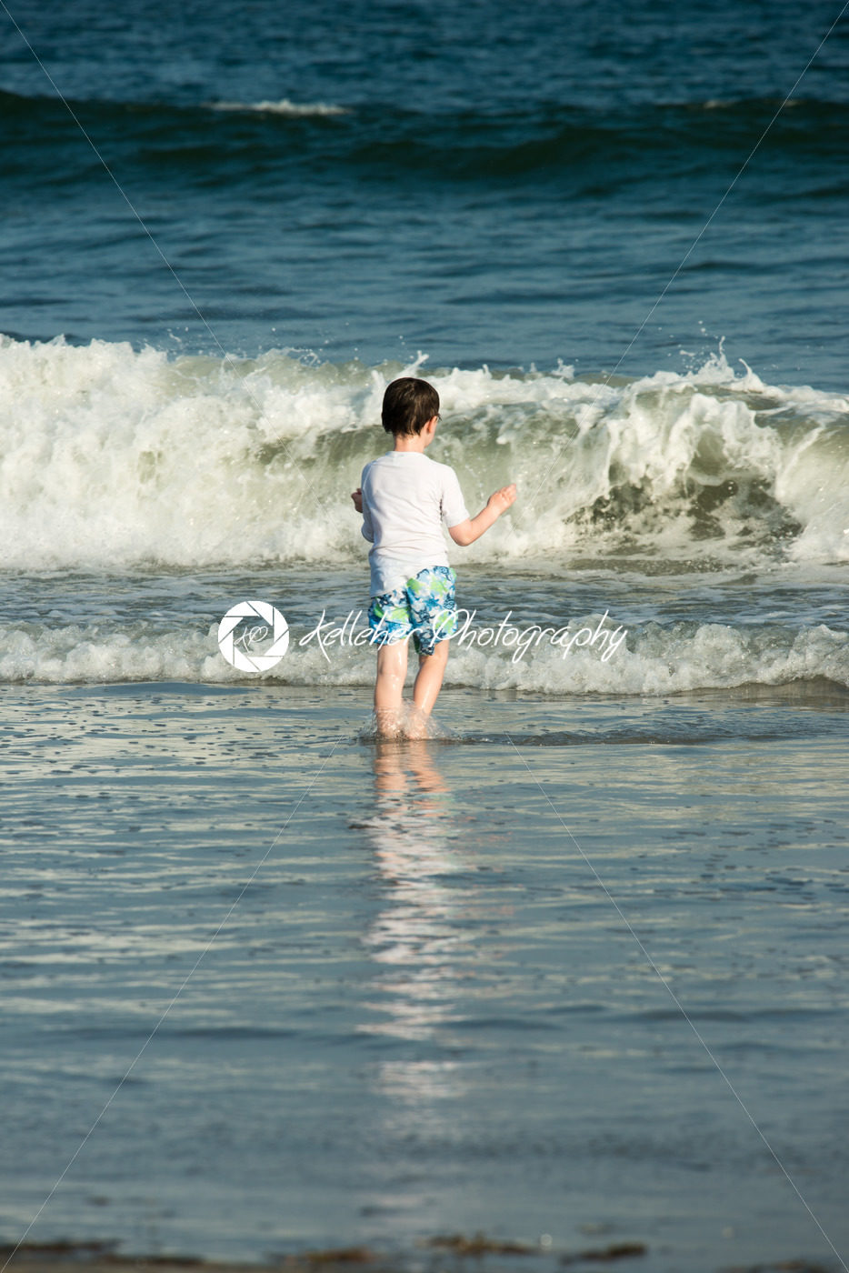 Young cute little boy playing at the seaside running into the surf on a sandy beach in summer sunshine - Kelleher Photography Store