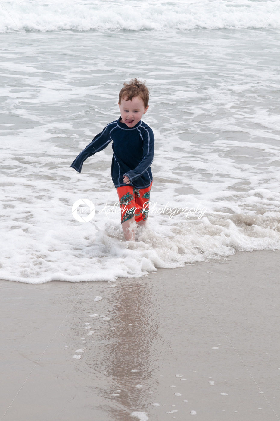 Young cute little boy playing at the seaside running into the surf on a sandy beach in summer sunshine - Kelleher Photography Store
