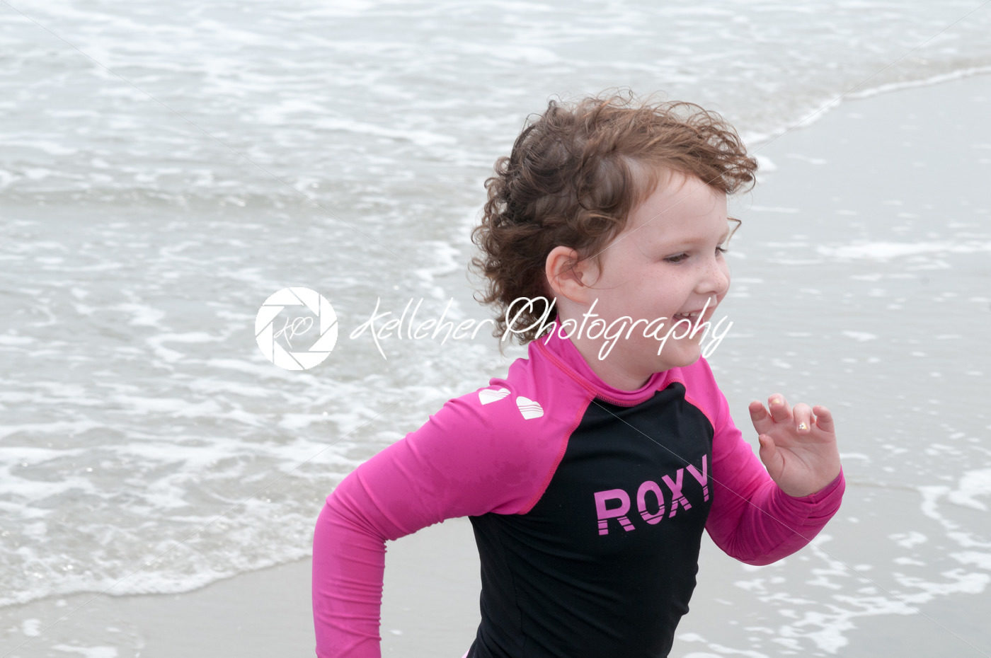 Young cute little girl playing at the seaside running into the surf on a sandy beach in summer sunshine - Kelleher Photography Store