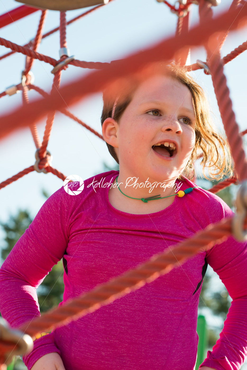 Young girl child playing at outdoor playground climbing net - Kelleher Photography Store