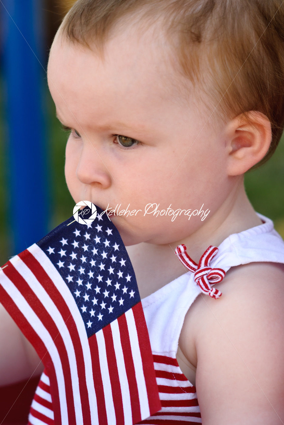 Young girl holding an American flag and riding in red wagon having fun in the park for July Fourth - Kelleher Photography Store