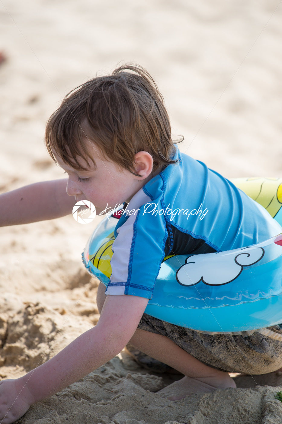 Young little boy playing with the sand and building sandcastle at the beach near the bay. - Kelleher Photography Store