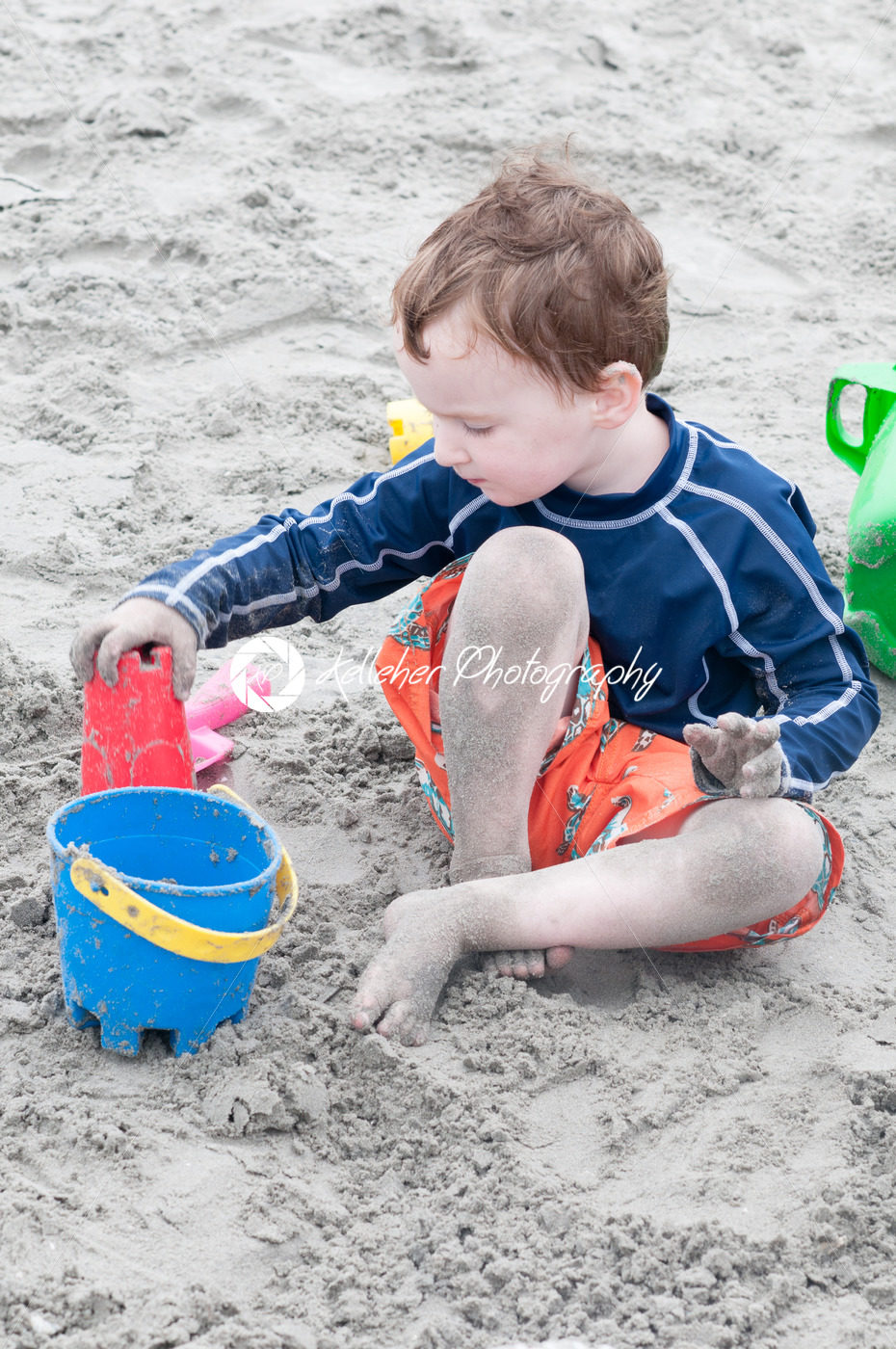 Young little boy playing with the sand and building sandcastle at the beach near the sea. - Kelleher Photography Store