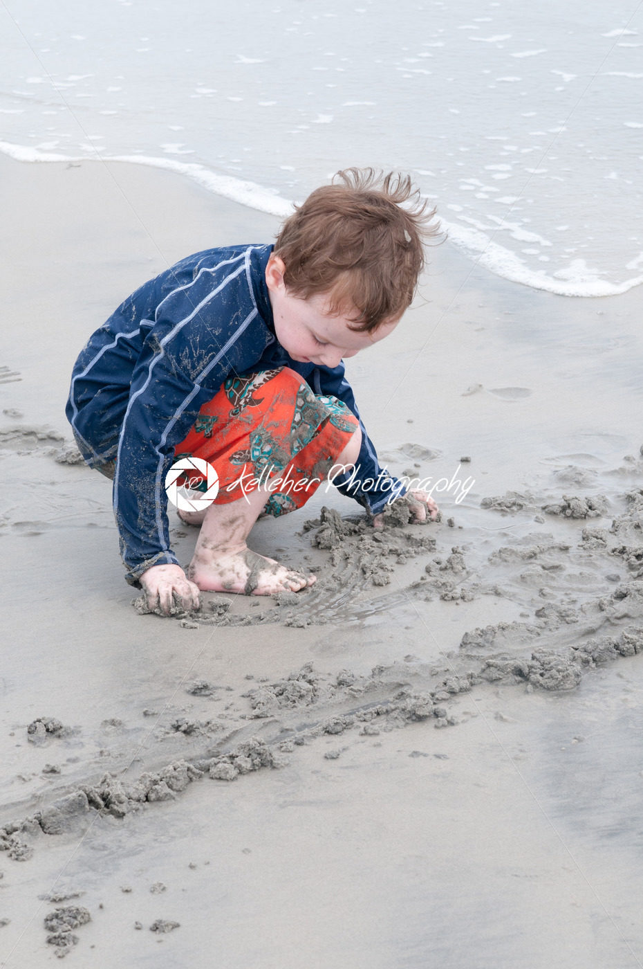 Young little boy playing with the sand and building sandcastle at the beach near the sea. - Kelleher Photography Store