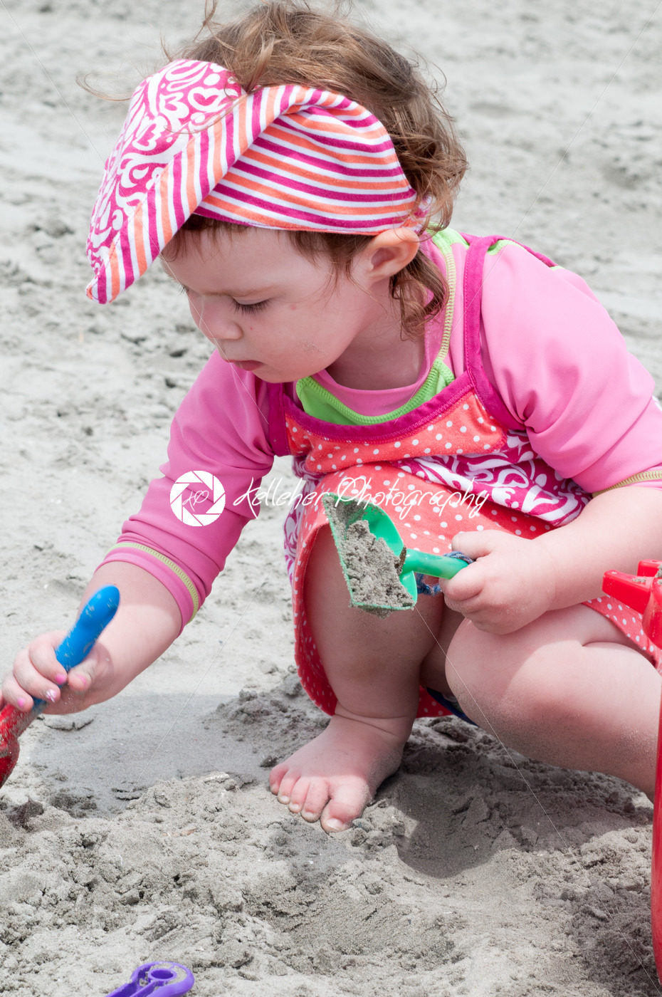 Young little girl playing with the sand and building sandcastle at the beach near the sea. - Kelleher Photography Store