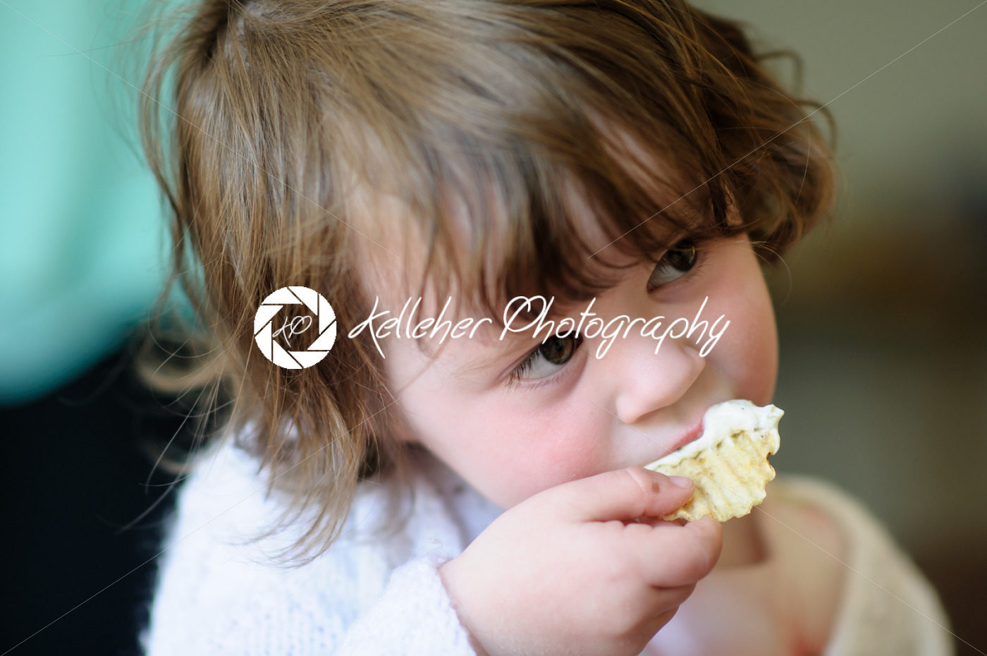 Portrait of a cute little girl inside eating potato chip with sour cream dip on it - Kelleher Photography Store