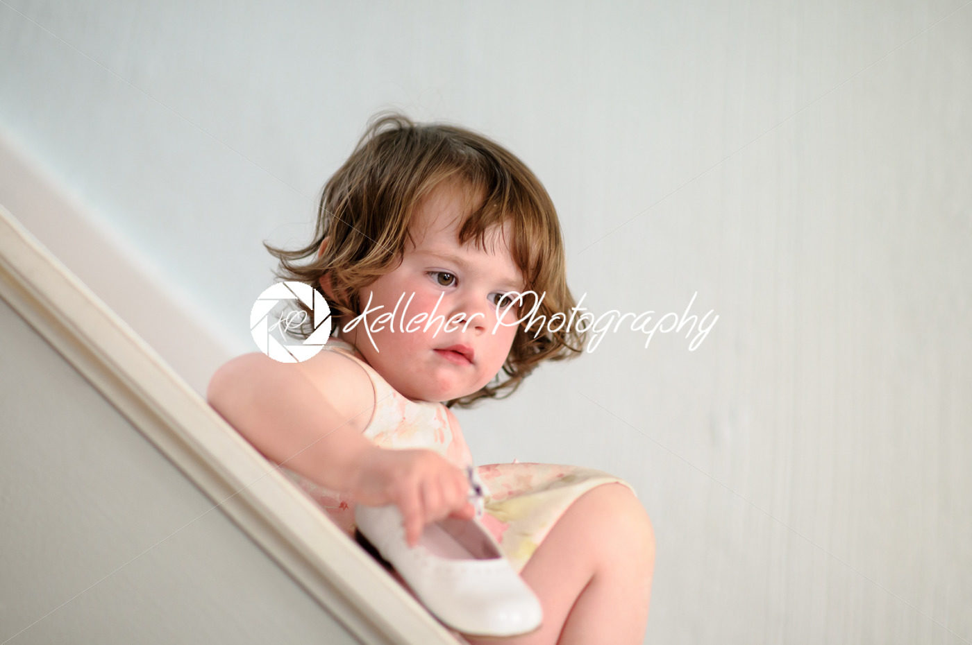 Portrait of a cute little girl inside on stairs holding dress show - Kelleher Photography Store
