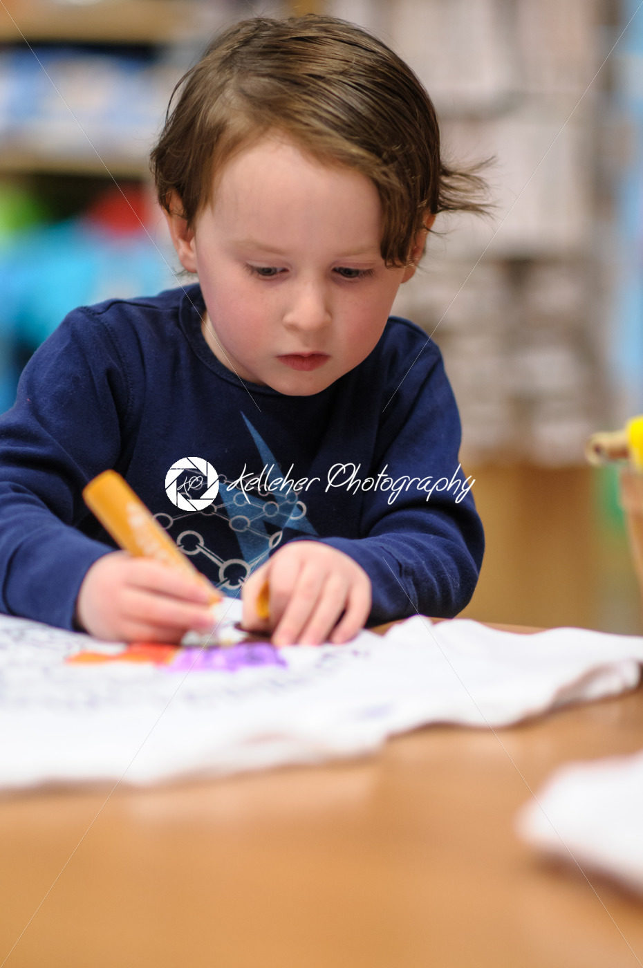 Young boy sitting down at desk indoors coloring with markers - Kelleher Photography Store