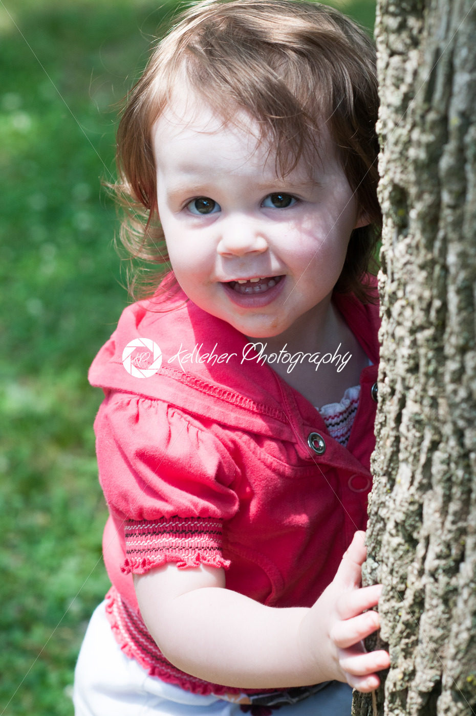 Young girl outside at park hugging standing next to tree - Kelleher Photography Store