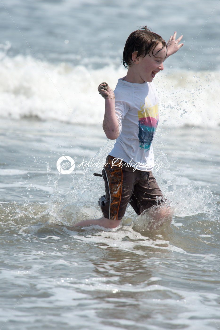 A happy young boy child running playing and having fun in the surf and waves of a sandy sunny beach - Kelleher Photography Store