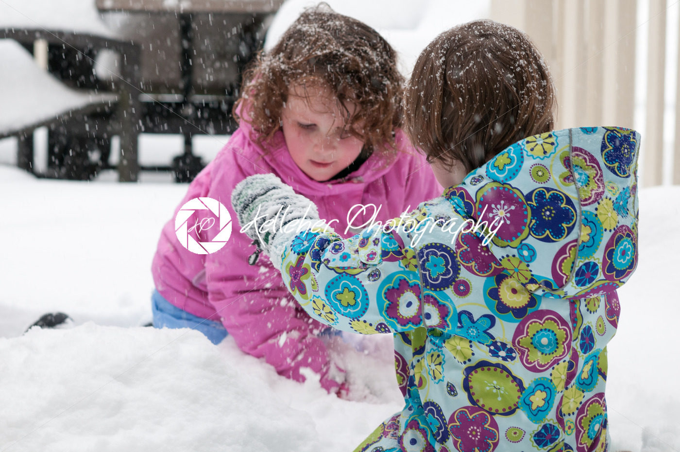 Happy toddler sibling girls in warm coat and knitted hat tossing up snow and having a fun in the winter outside, outdoor portrait - Kelleher Photography Store