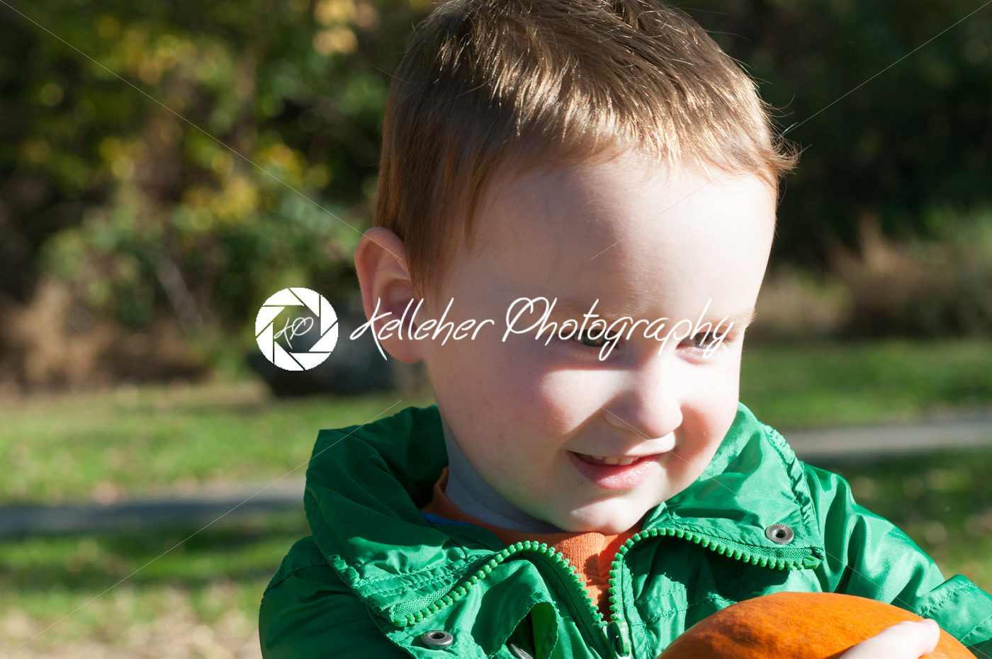 Young toddler boy outside holding a pumpkin with pumpkin fields in the background - Kelleher Photography Store