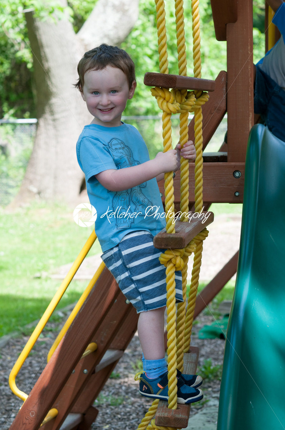 Happy little child boy climbing on the rope ladder outside - Kelleher Photography Store