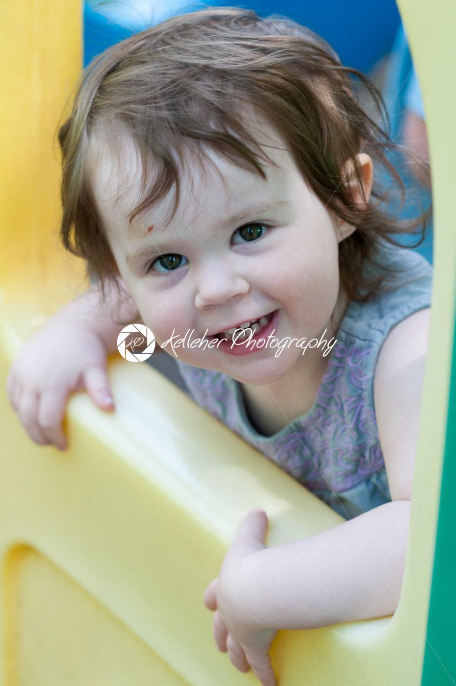 Little girl wearing summer dress looking out from plastic play house window in a playground - Kelleher Photography Store