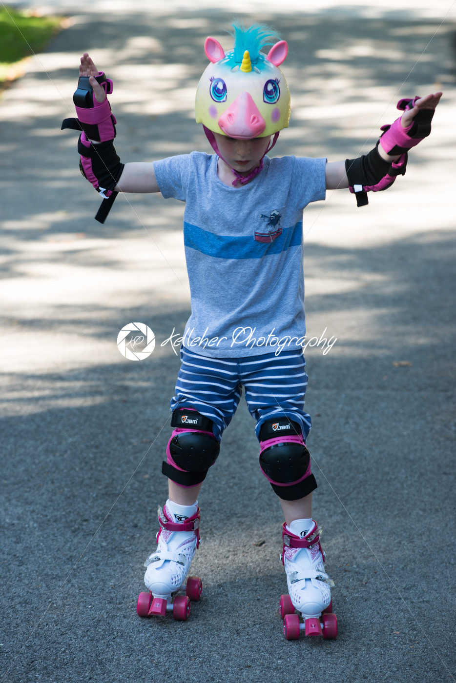 Young boy outside learning to riding on roller skates on driveway wearing protective helmet and elbow, wrist and knee pads - Kelleher Photography Store
