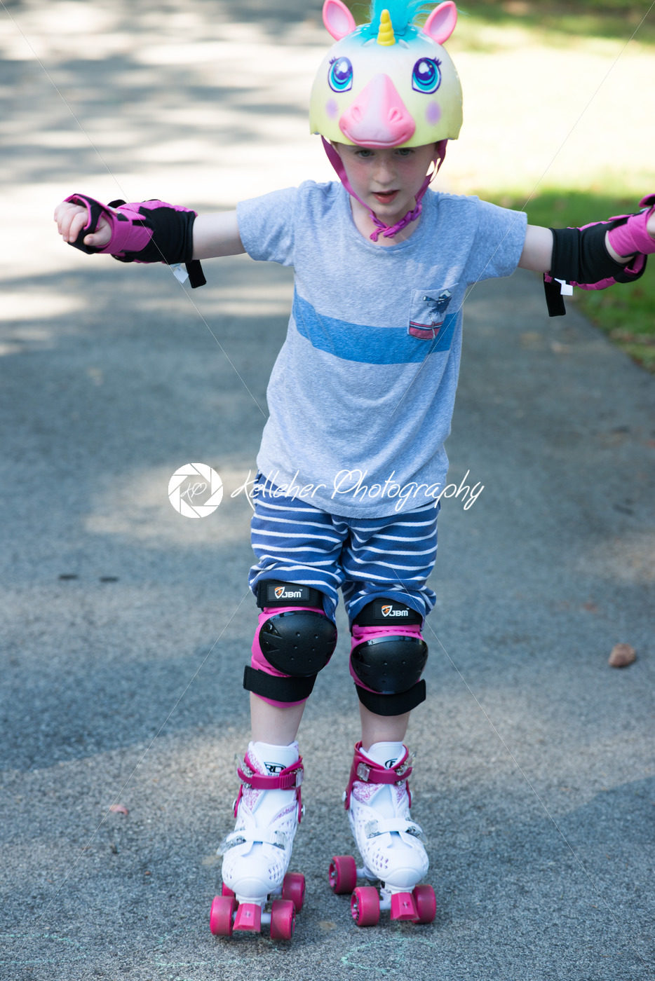 Young boy outside learning to riding on roller skates on driveway wearing protective helmet and elbow, wrist and knee pads - Kelleher Photography Store
