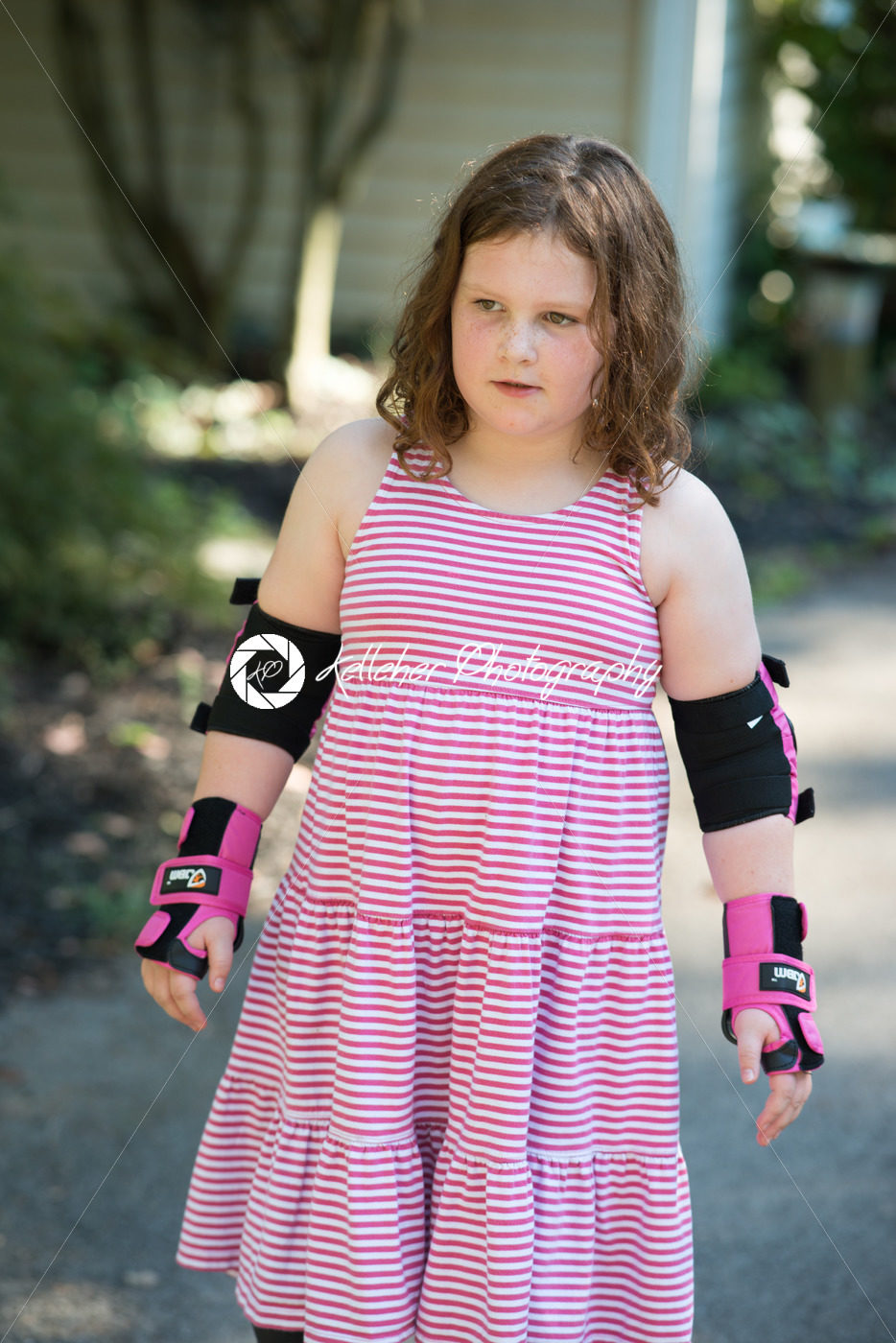Young girl outside learning to riding on roller skates on driveway wearing protective elbow, wrist and knee pads - Kelleher Photography Store