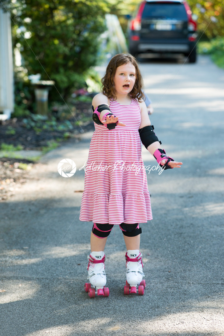 Young girl outside learning to riding on roller skates on driveway wearing protective elbow, wrist and knee pads - Kelleher Photography Store