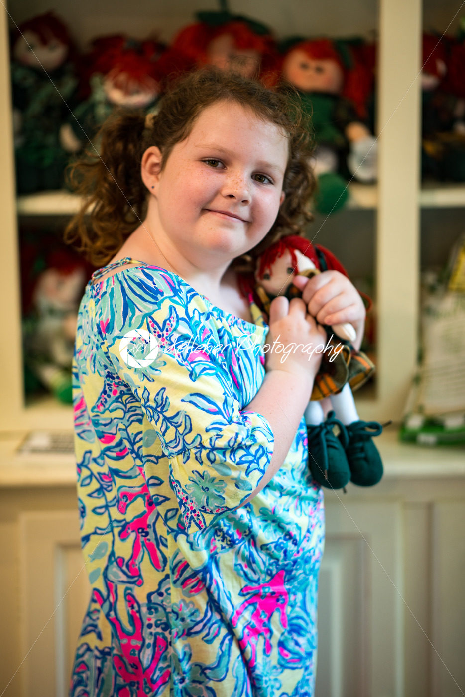 Young little Irish red-headed girl portrait looking and smiling at the camera holding doll that looks like herself - Kelleher Photography Store