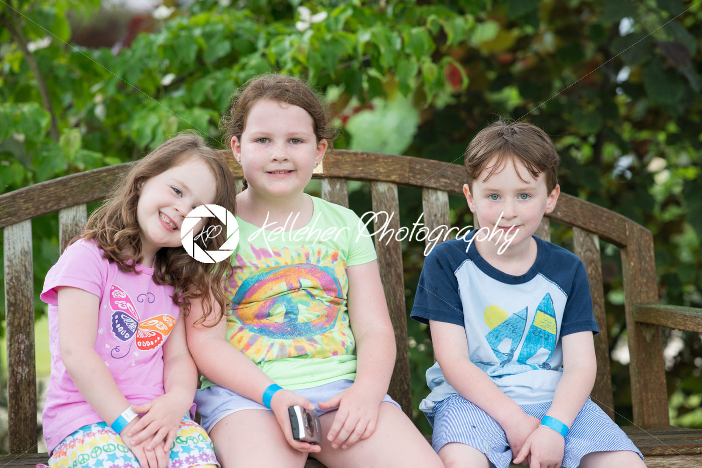 Three young siblings sitting on bench outdoors - Kelleher Photography Store