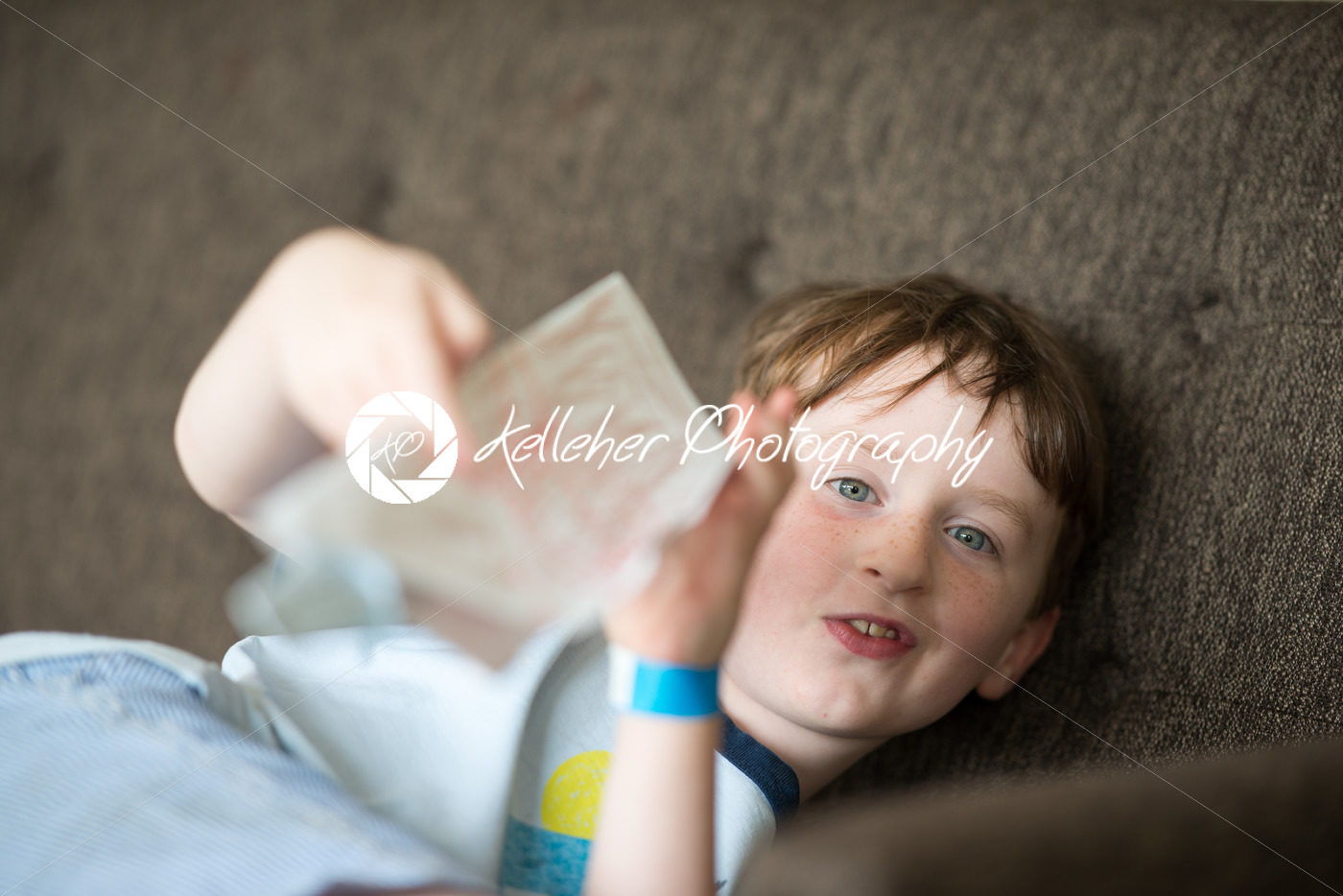 Young boy lying relaxing on a sofa while reading - Kelleher Photography Store