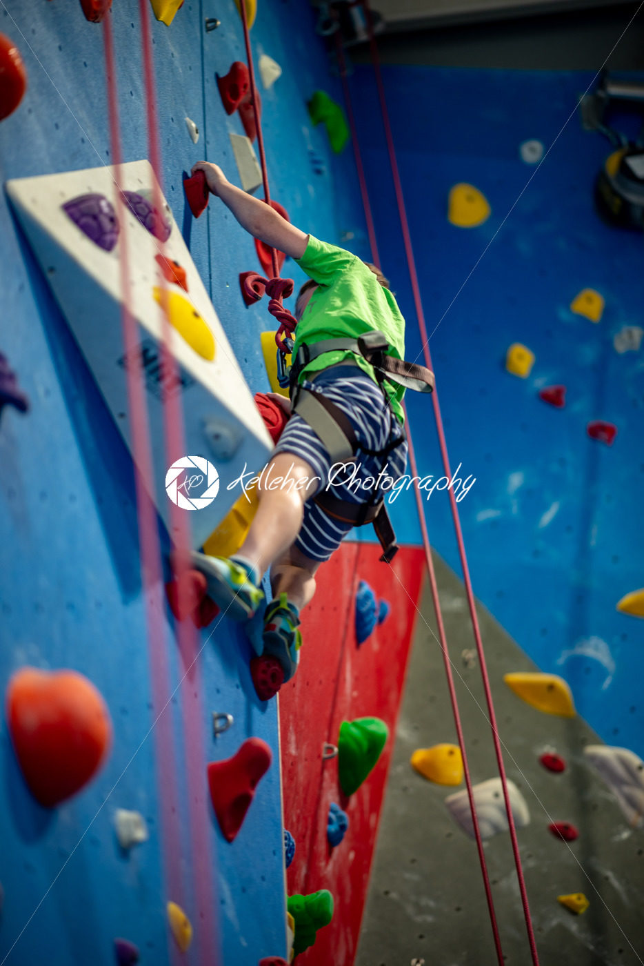 Young boy climbing up on practice wall in indoor rock gym - Kelleher Photography Store