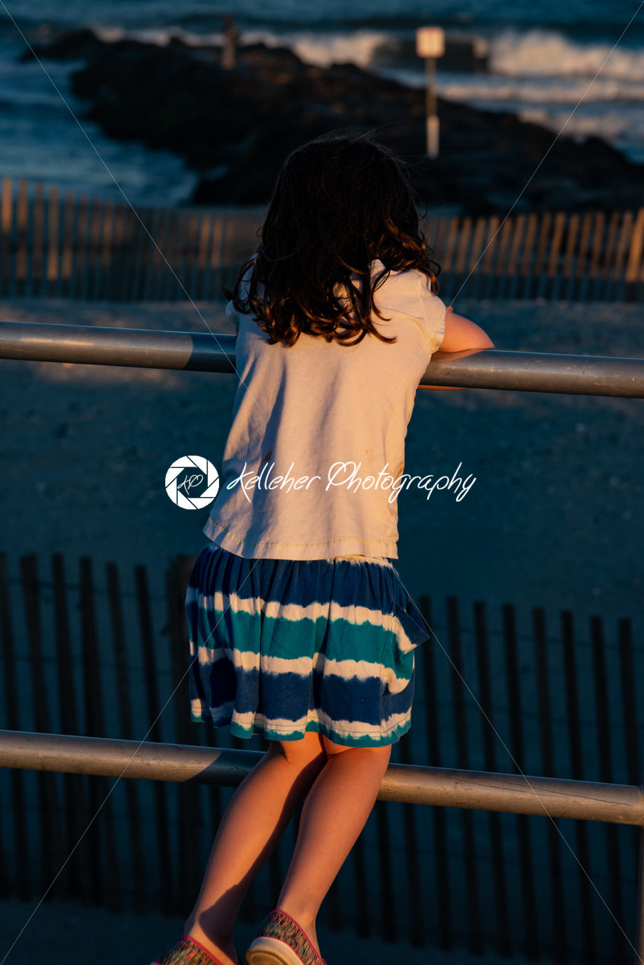 Young cute little girl on the boardwalk with back to camera looking towards the ocean surf - Kelleher Photography Store