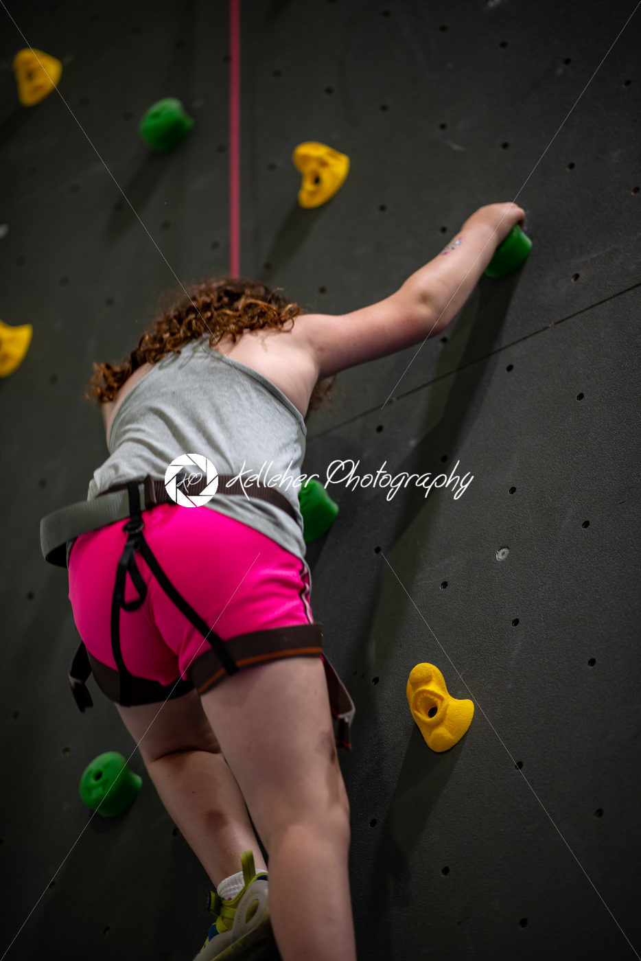 Young girl climbing up on practice wall in indoor rock gym - Kelleher Photography Store