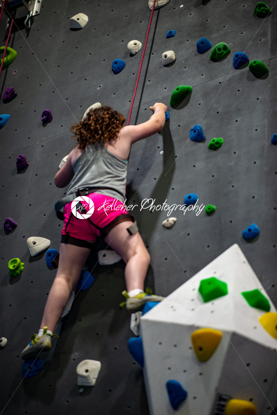 Young girl climbing up on practice wall in indoor rock gym - Kelleher Photography Store